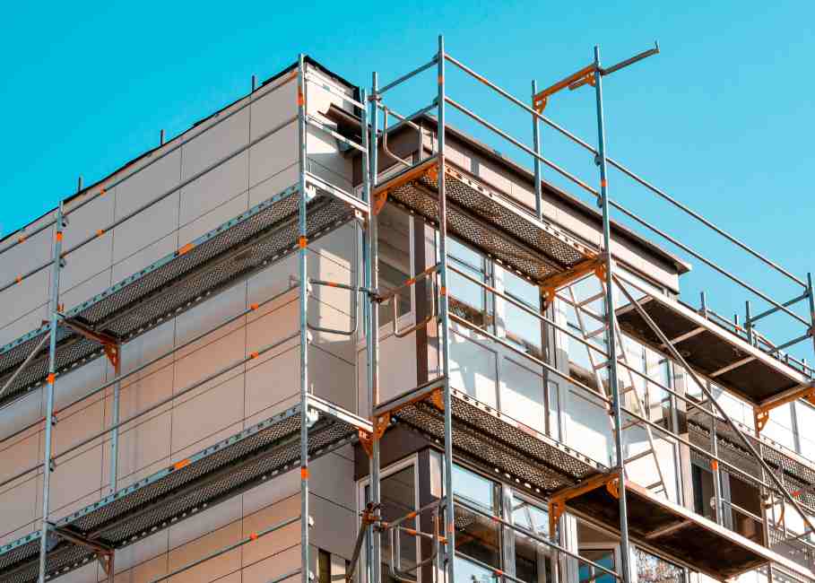 Fachada de edificio en proceso de rehabilitación con andamios y paneles de aislamiento térmico bajo un cielo azul.