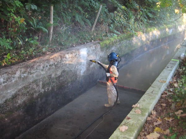 impermeabilizacion poliurea spray Aplicación de poliurea proyectada por un operario en un canal de hormigón para su impermeabilización.
