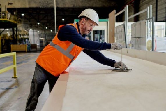 Operario manipulando XPS_reducida Operario midiendo y cortando paneles de aislamiento XPS en una nave industrial.