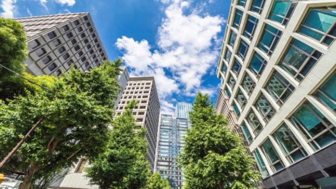 Edificios residenciales y de oficinas con fachadas acristaladas rodeados de árboles bajo un cielo azul, símbolo de eficiencia y sostenibilidad urbana.